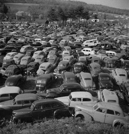 A black and white shot of a field of old, broken down cars.