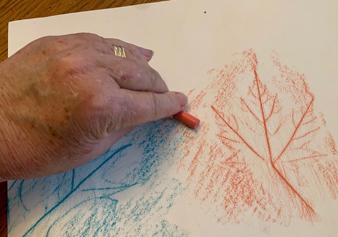 An example of a leaf rubbing onto a white piece of paper using an orange crayon