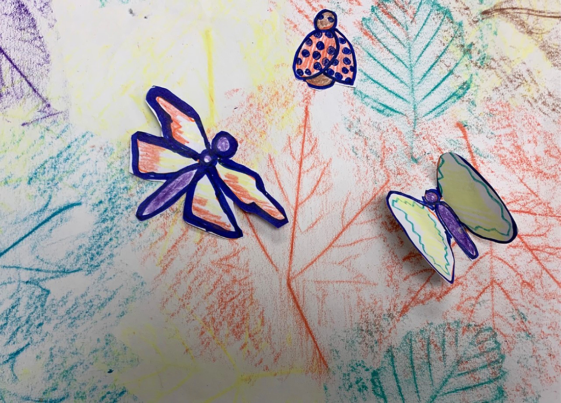 Cutout drawings of a dragonfly, ladybug, and butterfly glued on top of a colorful leaf rubbing drawing