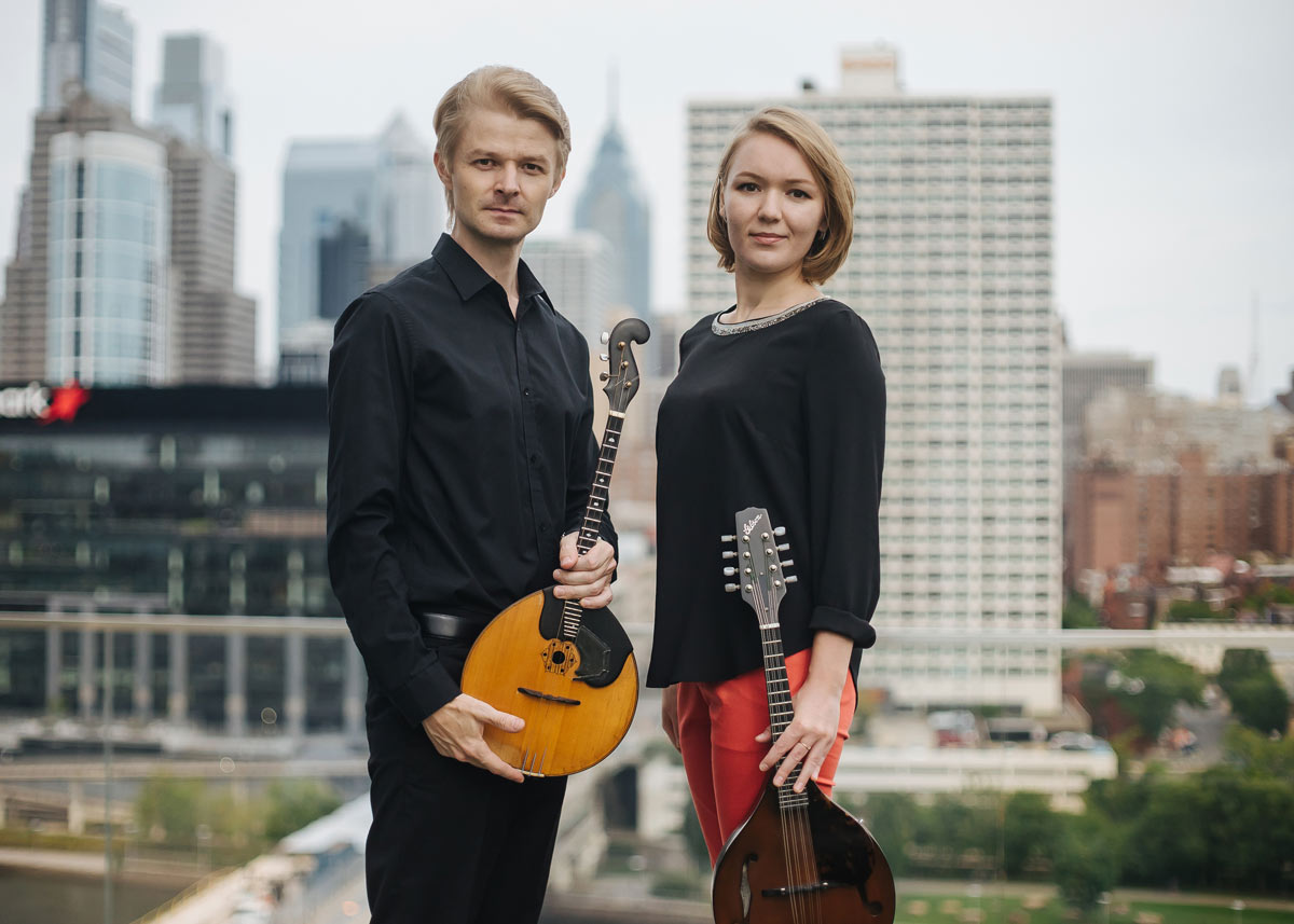 Photo of two musicians with a cityscape in the background.