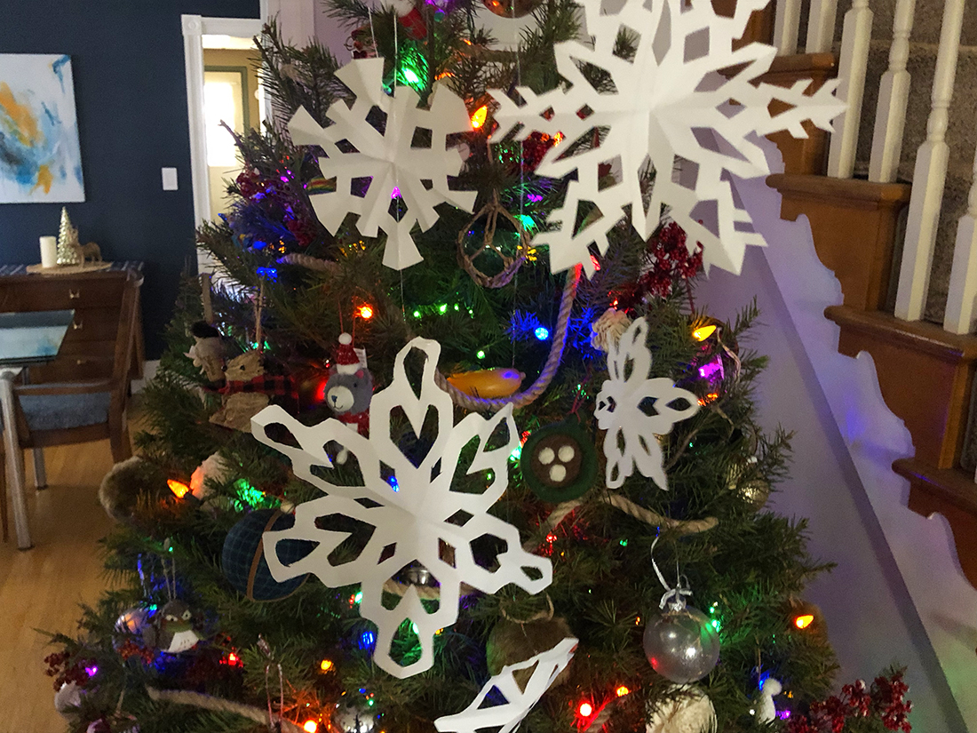 Paper snowflakes hung up in front of a Christmas tree