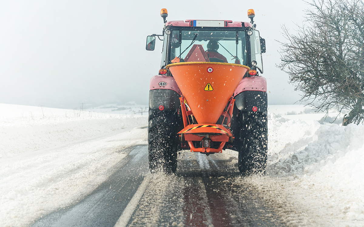 Snow plow spreading de-icing road salt onto highway