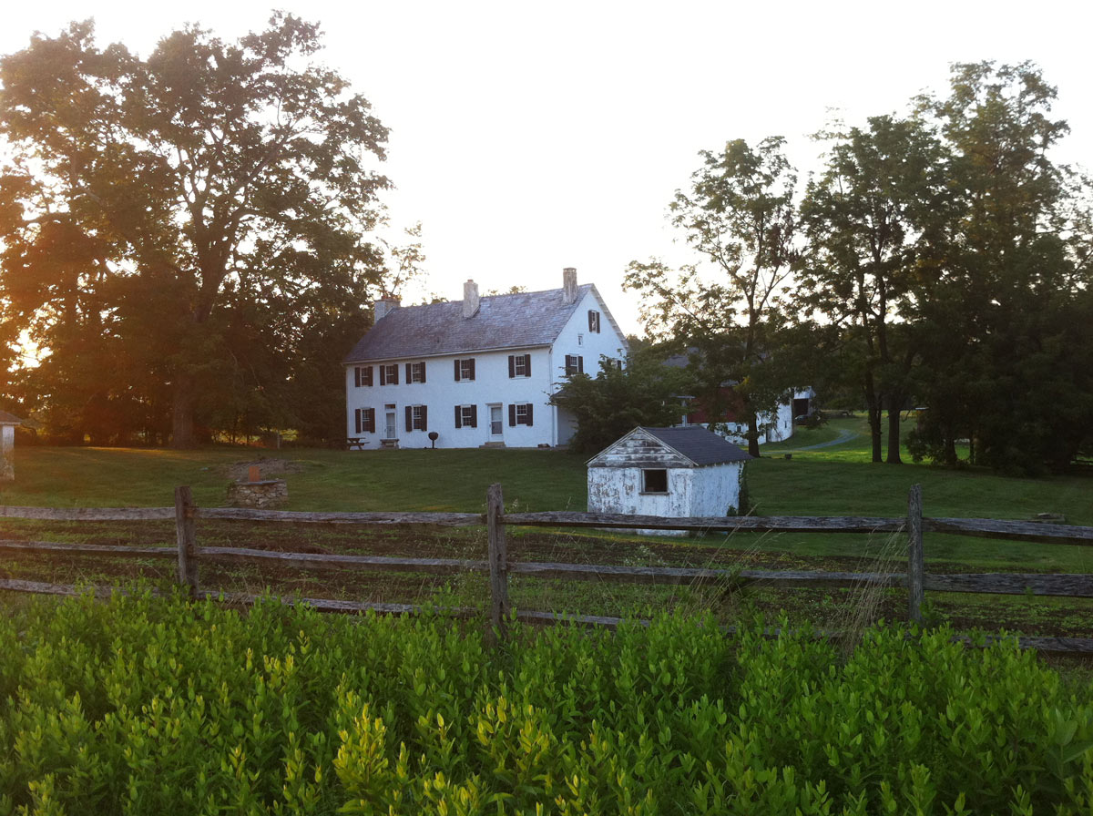 Field with a wood fence and white farmhouse in the background.