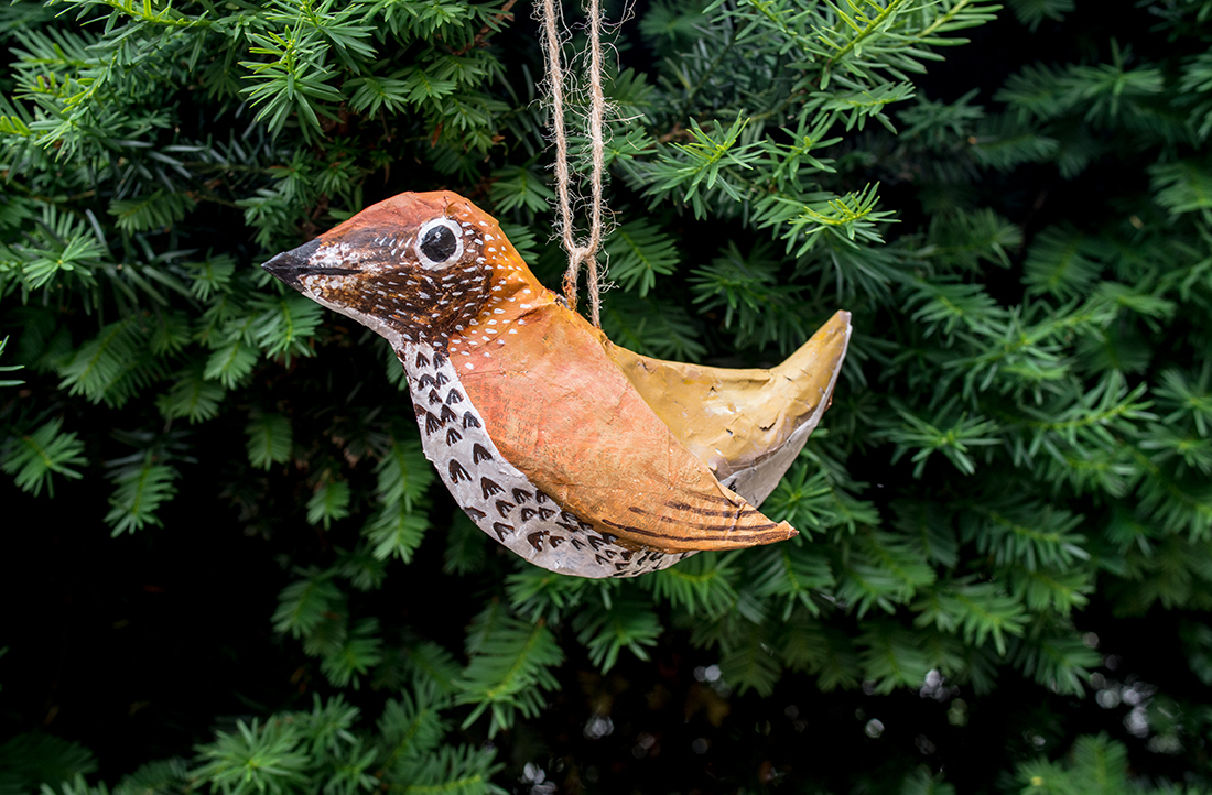 Colorful Papier-Mâché bird hanging in front of some green tree branches