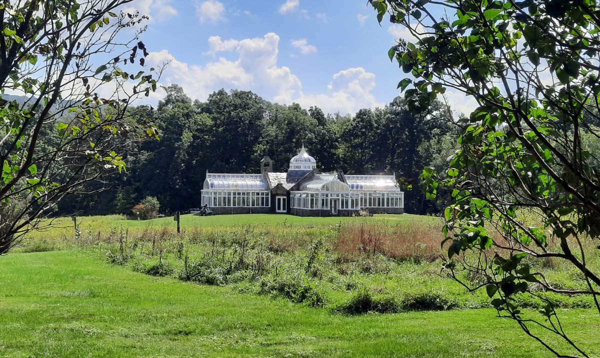 A greenhouse in a field with trees and native plants in the foreground.
