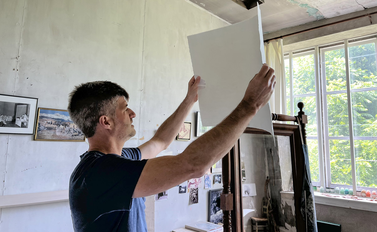 A person holding watercolor paper in the air to look closely at it.