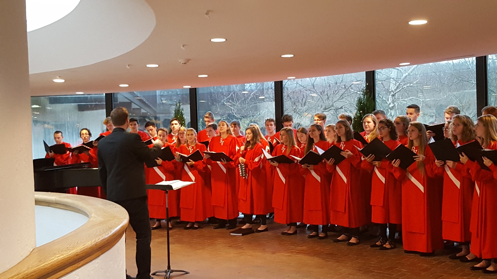 School choir wearing red choir robes, arranged in a half circle formation in the Museum's atrium