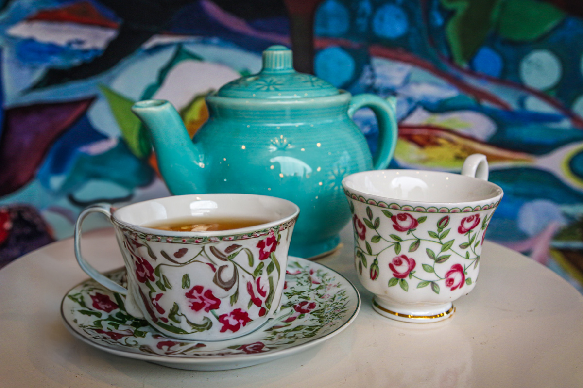 tea cups with a green tea pot in front of a patterned background.