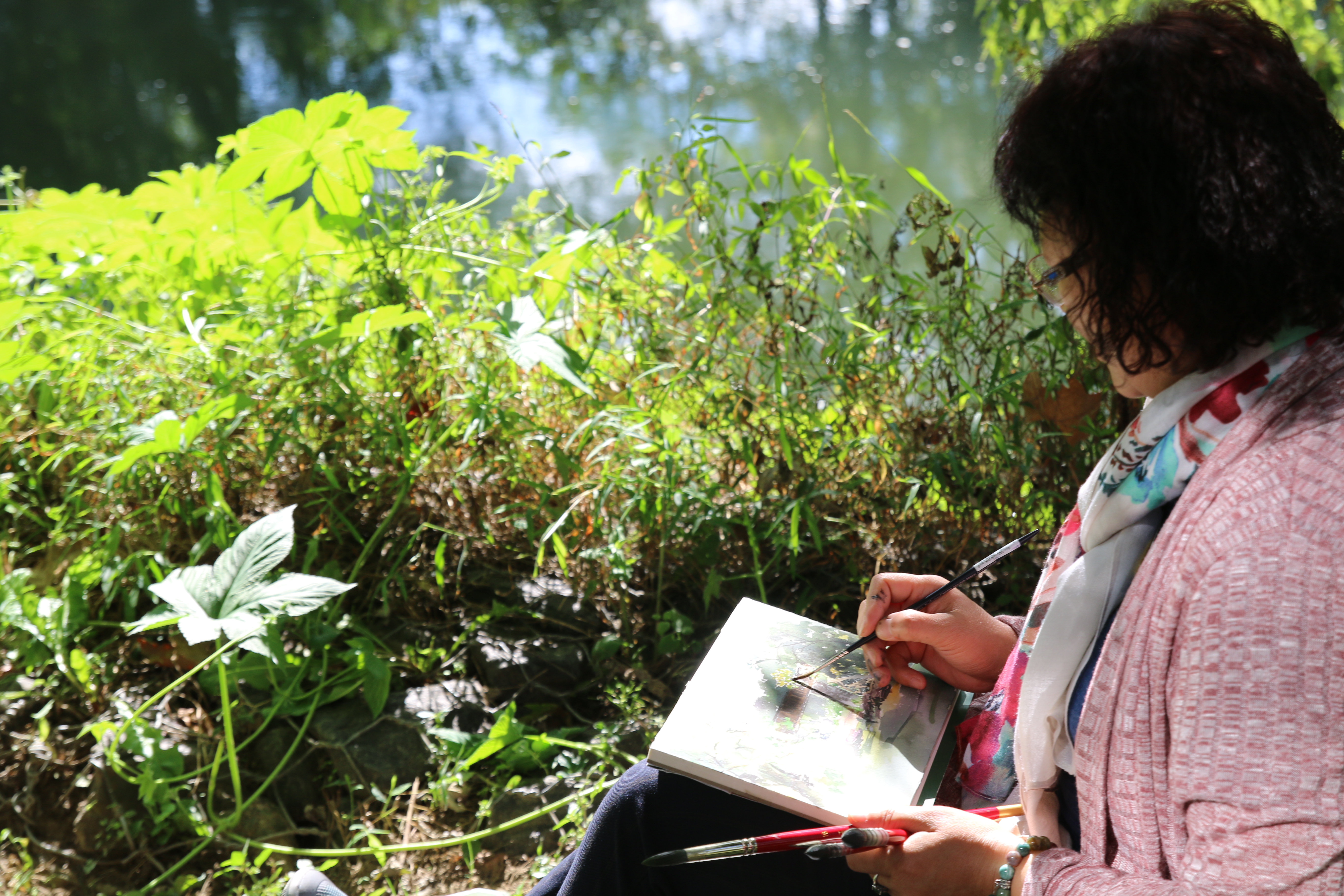 A woman sits and sketches in a notebook on a summer day.