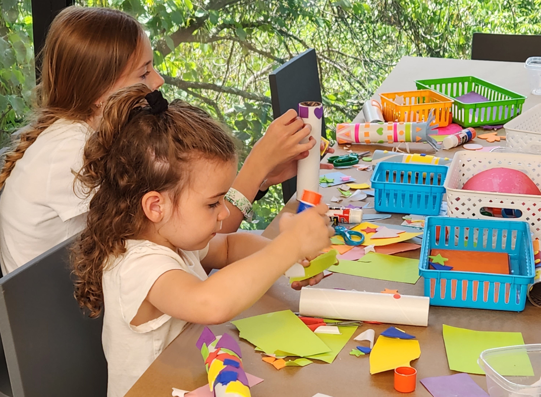 A young girl crafting at a table with colorful paper.