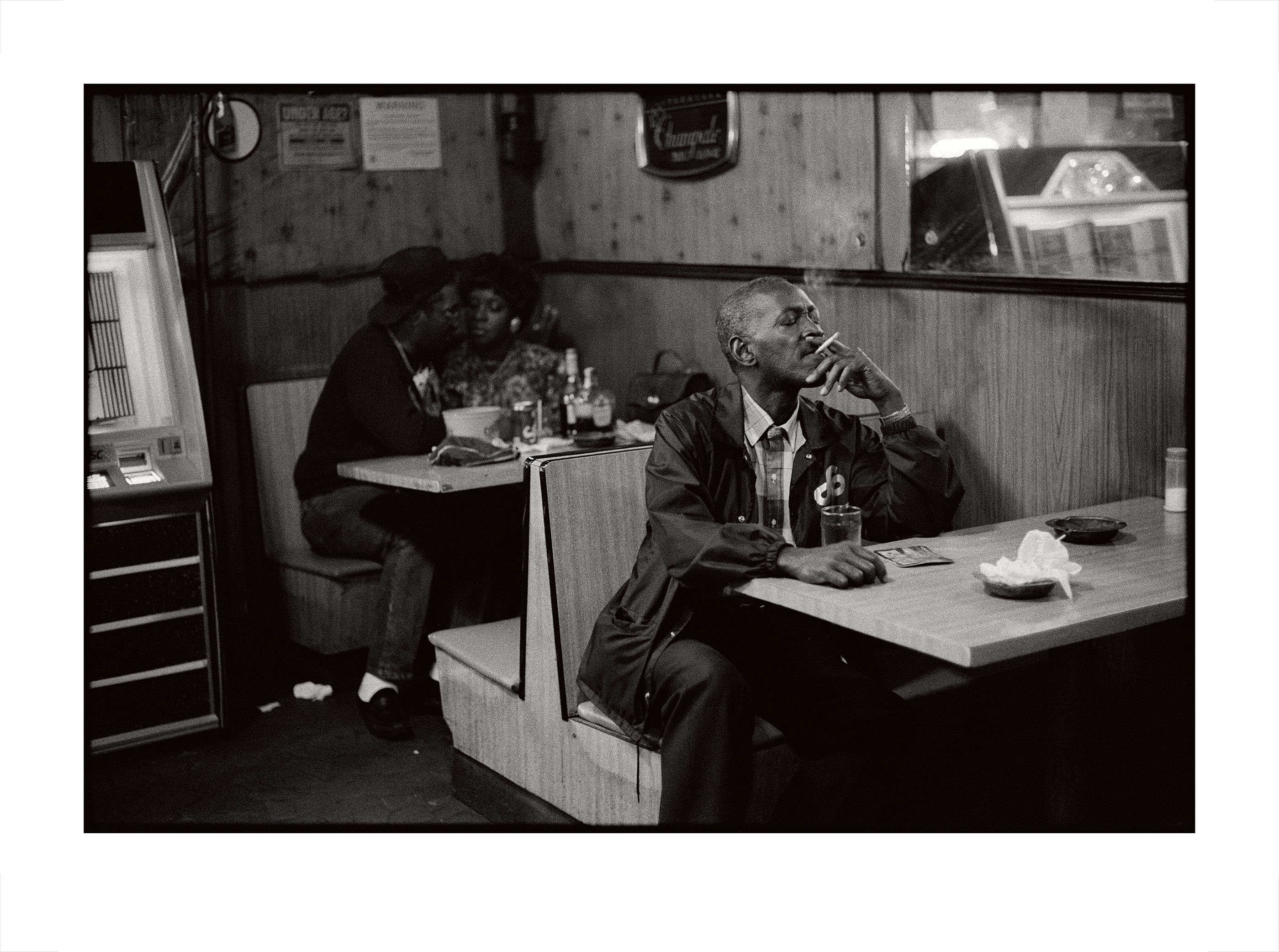 Black-and-white photograph of people sitting in booths inside of a restaurant