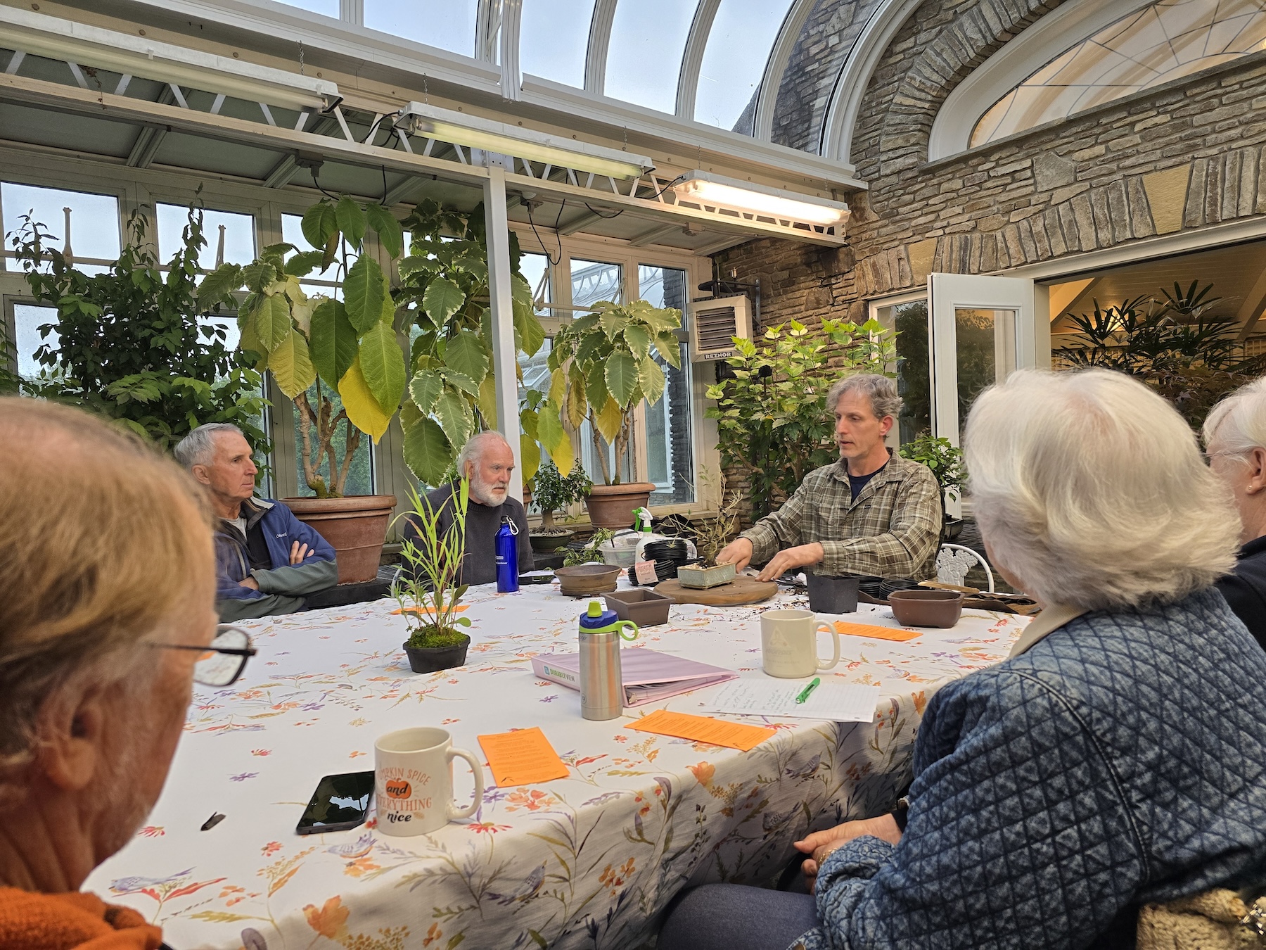 A group of people sitting at a large table creating Bonsai arrangements