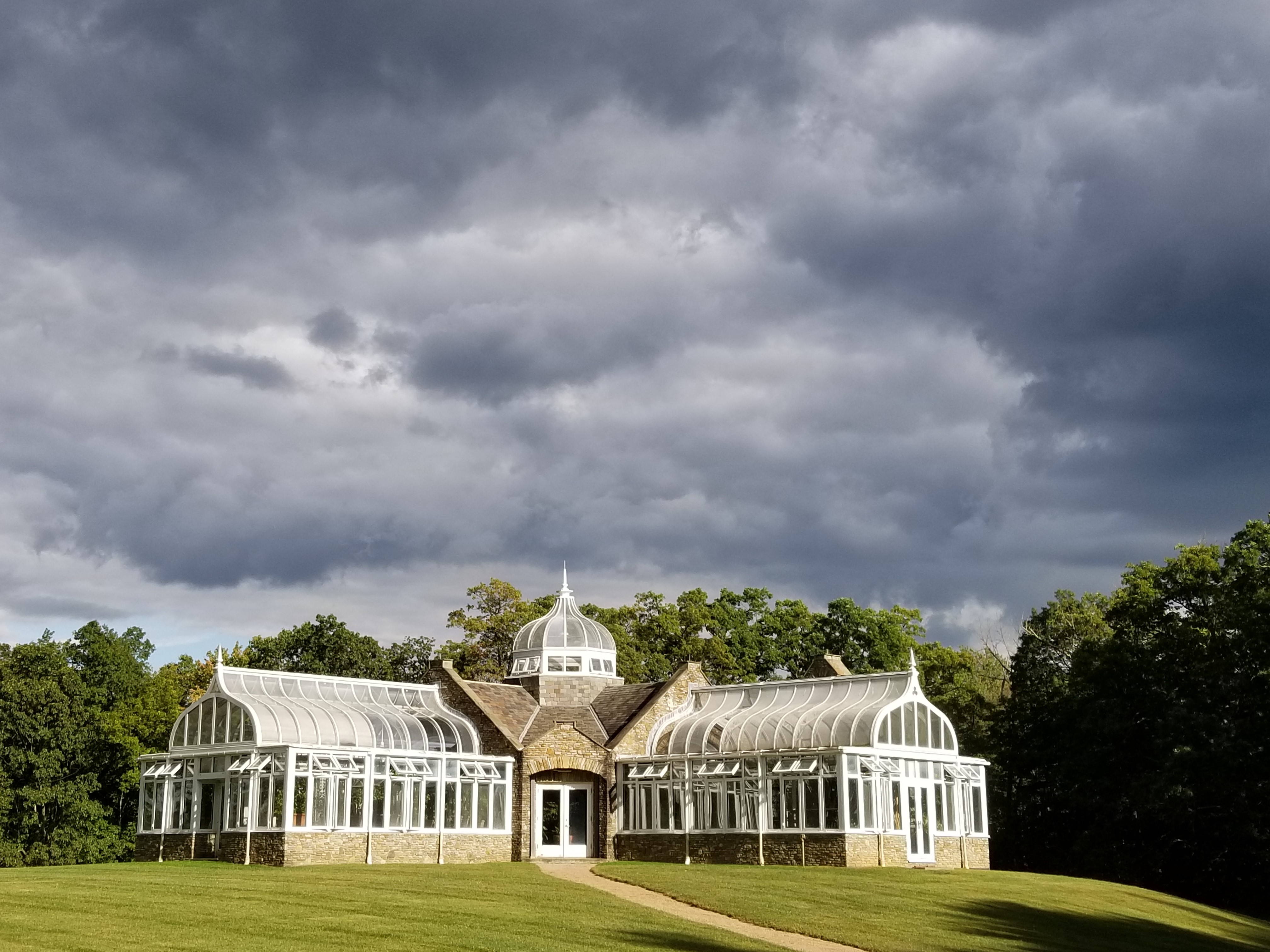A conservatory on a hill, with rain clouds in the background.