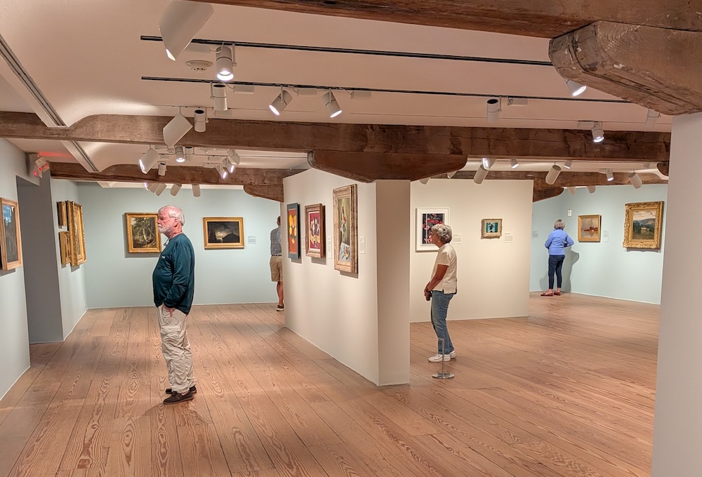 People standing around in an art gallery, looking at paintings.