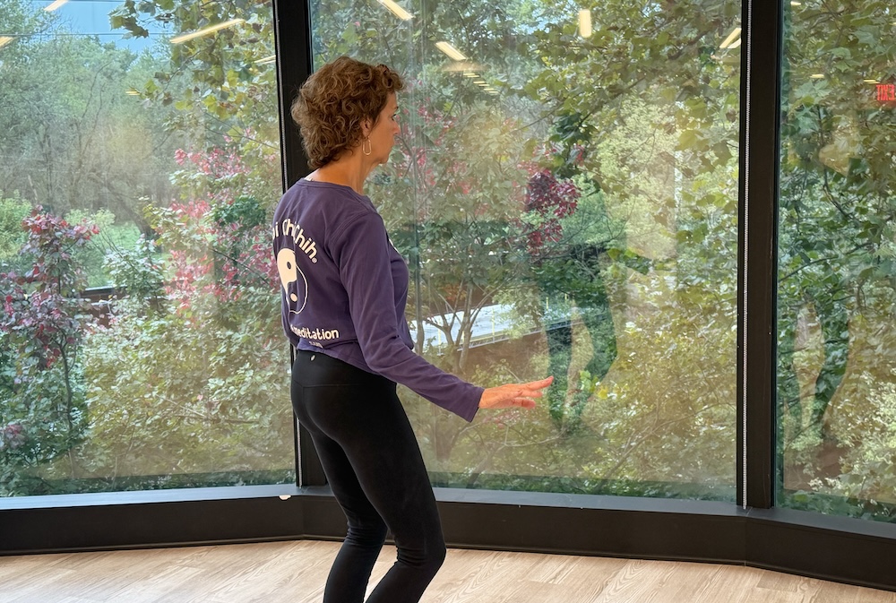 Woman standing in front of a large window doing T'ai chi chih