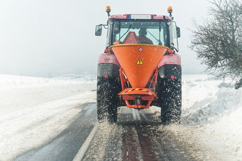 Snow plow spreading de-icing road salt onto highway