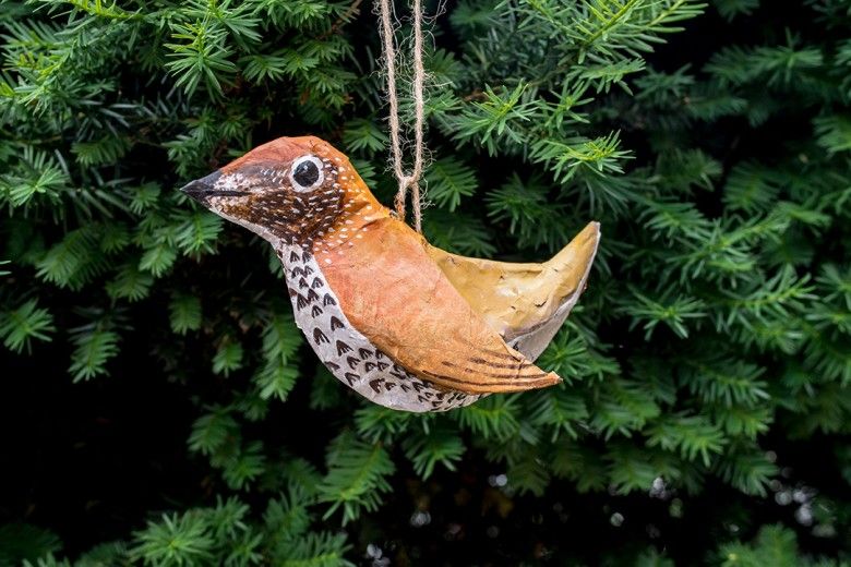 Colorful Papier-Mâché bird hanging in front of some green tree branches