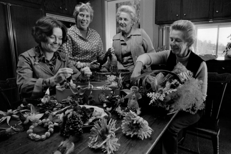Women gather around a table making holiday decorations