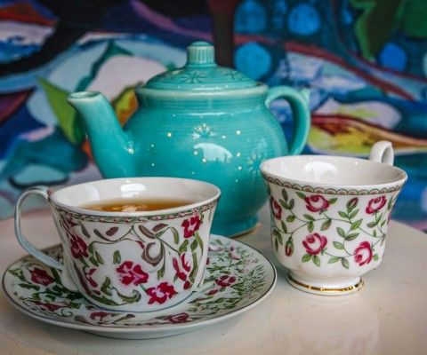 tea cups with a green tea pot in front of a patterned background.