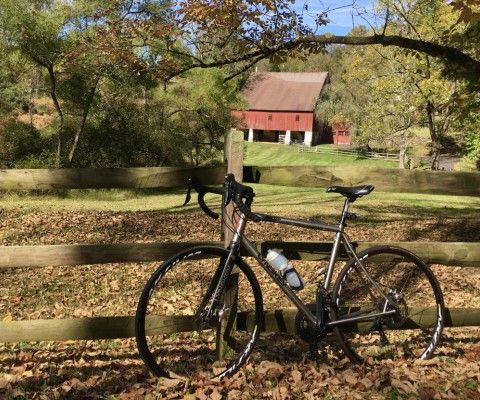 A bike leaning against a fence with a red barn in the background.