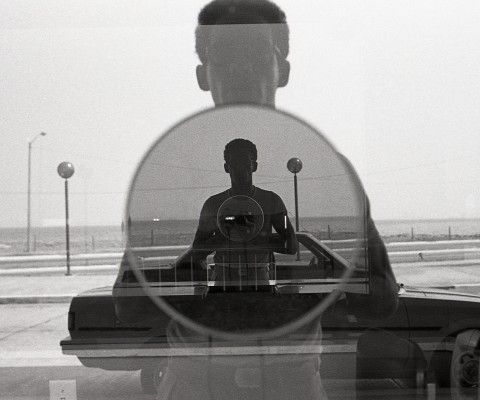 Black-and-white self-portrait photograph of a man and his reflection through a window