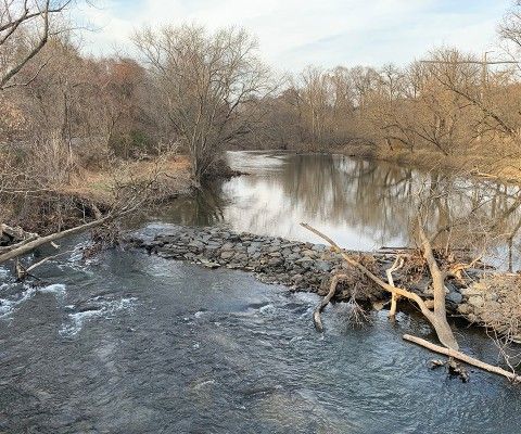 landscape photo of a low head dam seen from a bridge in winter