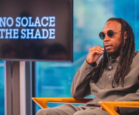 a man sitting, holding a microphone, talking to a crowd