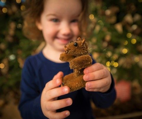 Girl holding a handmade Critter ornament in front of a Christmas Tree at the Brandywine River Museum of Art