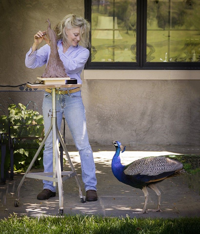 An artist sculpting a model of a peacock