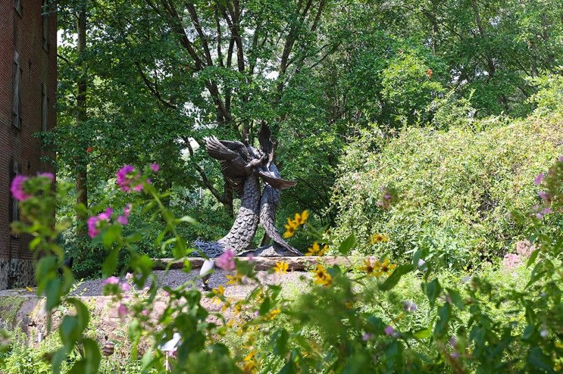 "Tipping Point" bronze sculpture seen in the distance with summer flowers blooming in front of it