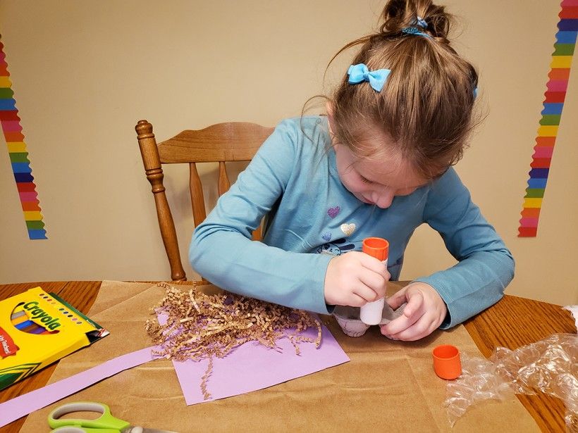 A young girl using a glue stick on a cut-up egg carton