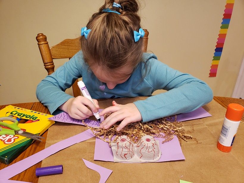 A young girl drawing on construction paper with a marker