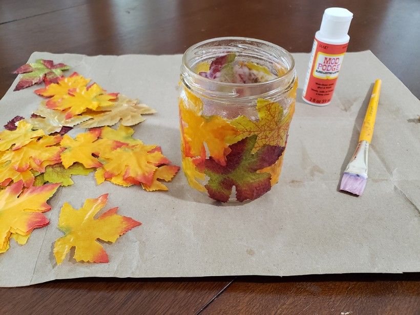 Fall leaf candle holder with a paintbrush, mod lodge container and extra leaves scattered on a table