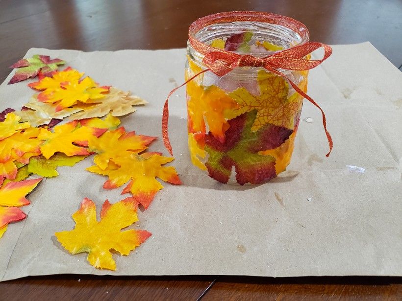 Fall leaf candle holder on a table with some extra leaves scattered around