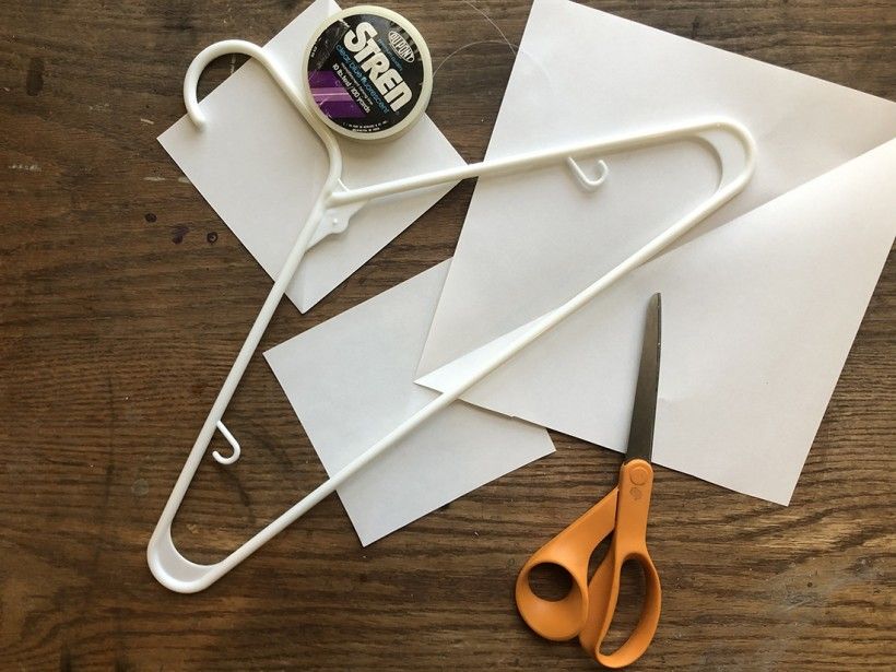 Photo of snowflake mobile supplies: three pieces of white paper, a white clothes hanger, a pair of scissors, and a roll of fishing line