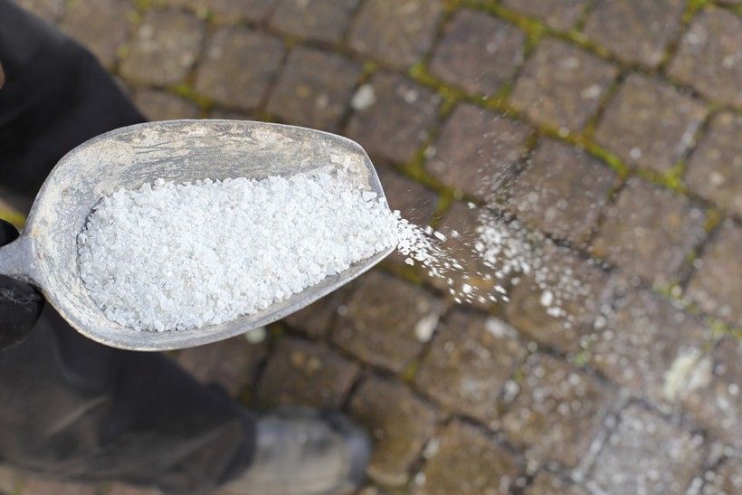 Road salt being sprinkled onto a stone pavement