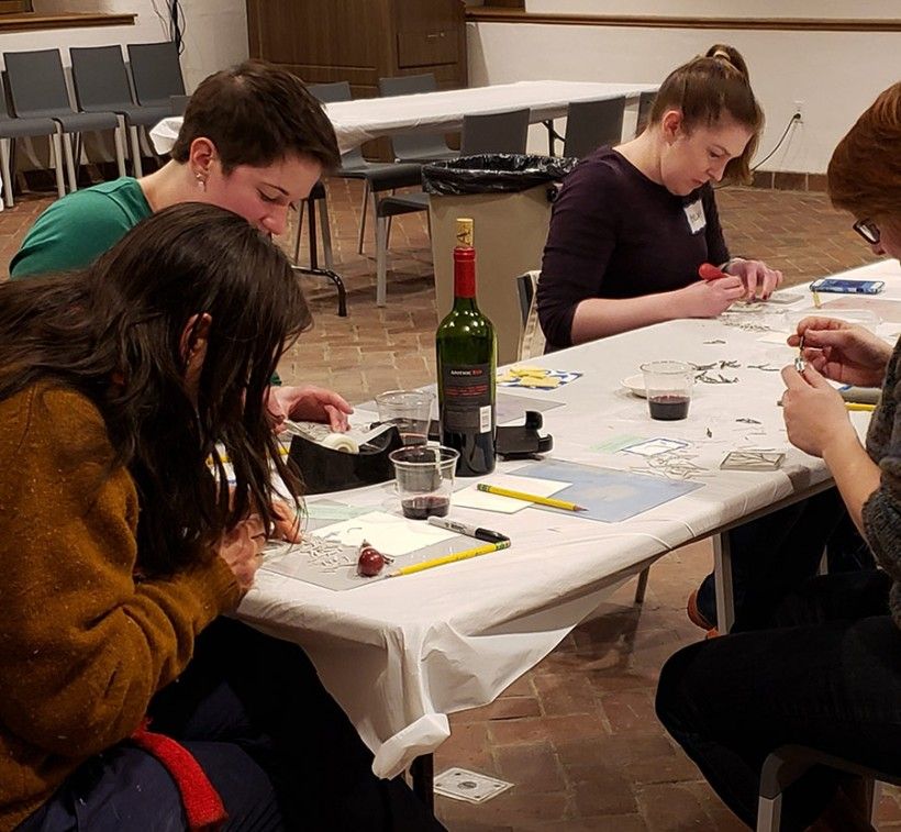 Group working on a craft project with a bottle of wine on the table.