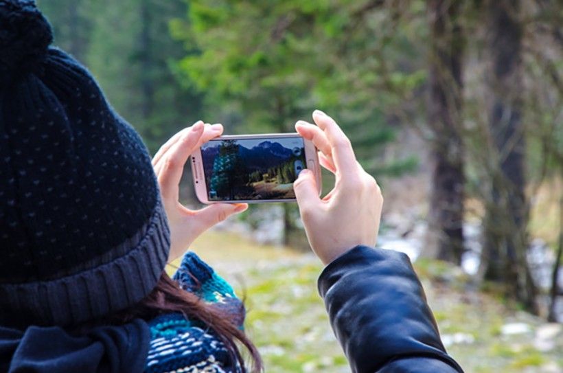 Woman taking a photo of trees with her phone.