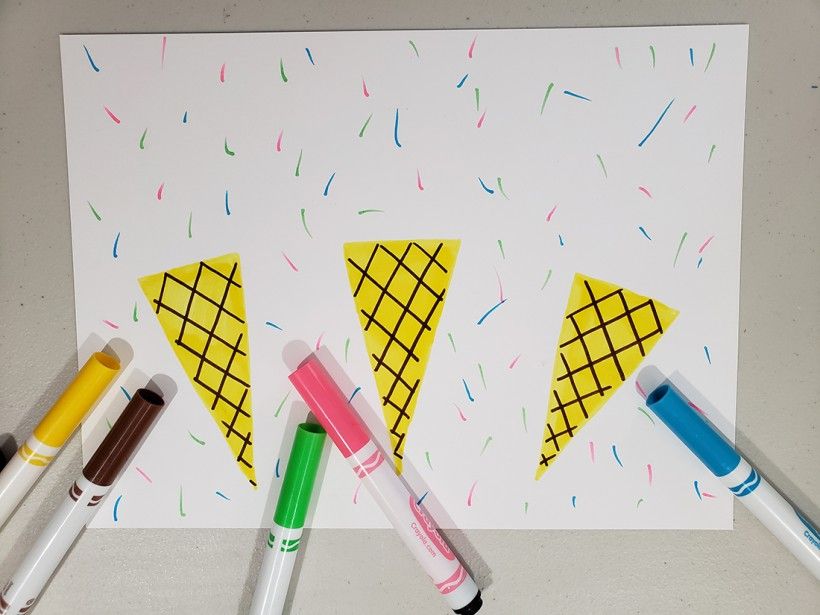 A piece of white paper with three yellow ice cream cone drawings and some colorful markers