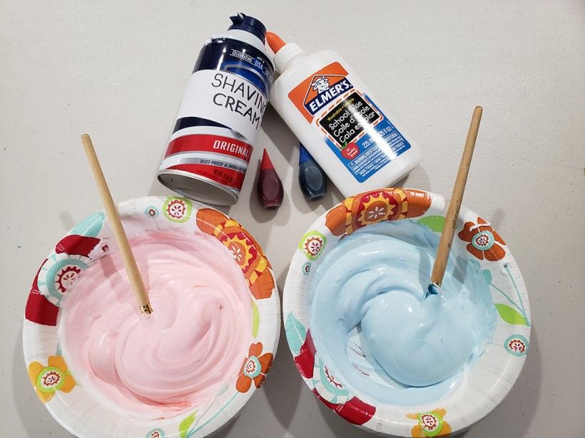 Two bowls filled with shaving cream that has been dyed pink and blue, being mixed up with a paintbrush.