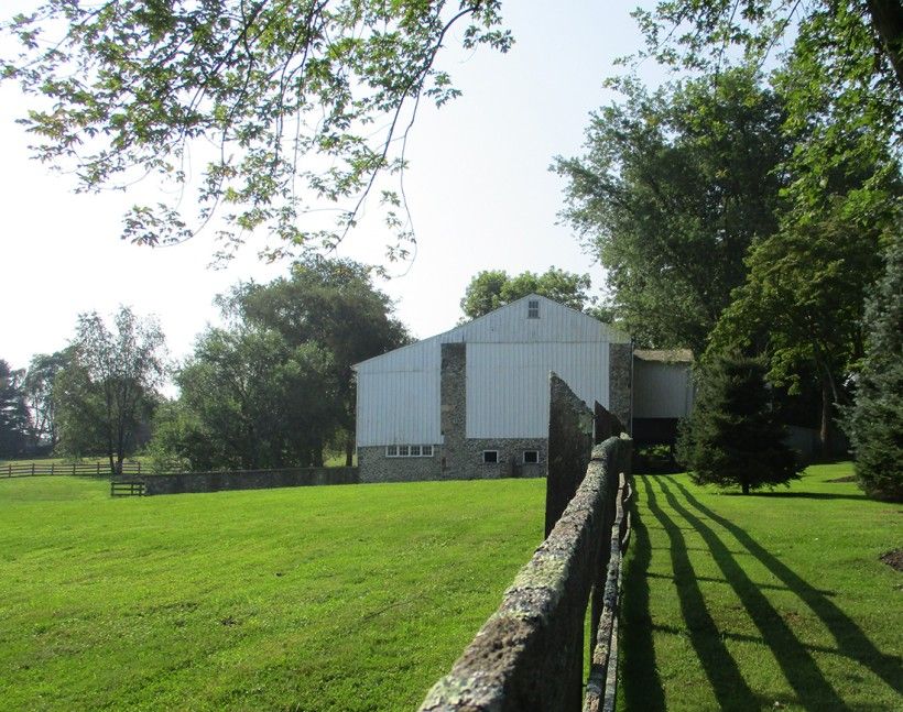 Farmhouse on a grassy field with trees and a fence.