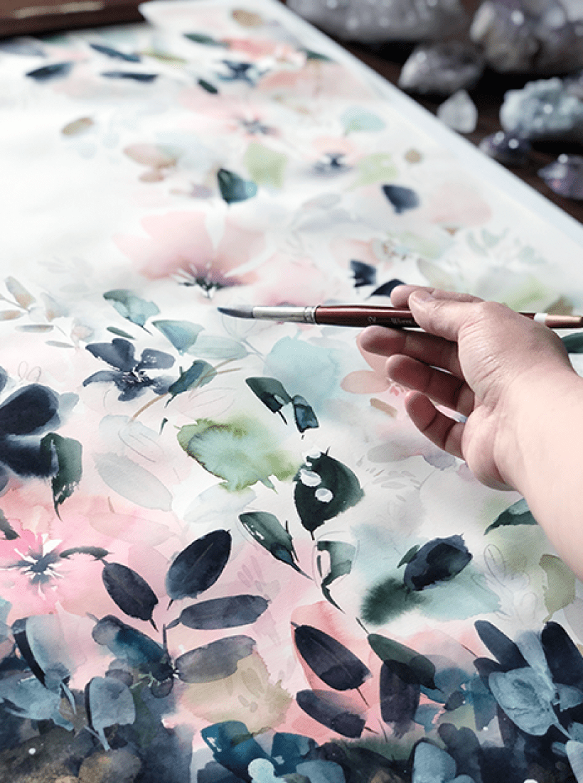 A hand holding a watercolor brush infant of a colorful painting