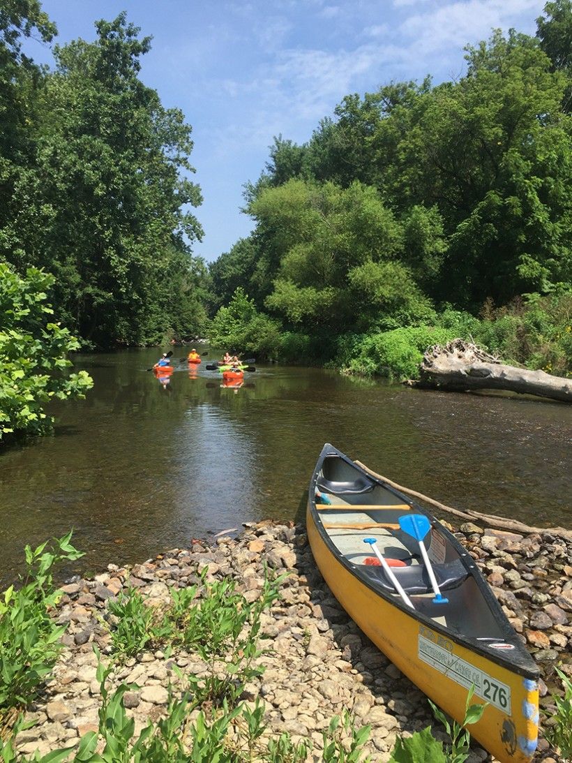 A canoe on a rocky piece of land overlooking a body of water lined with trees and greenery