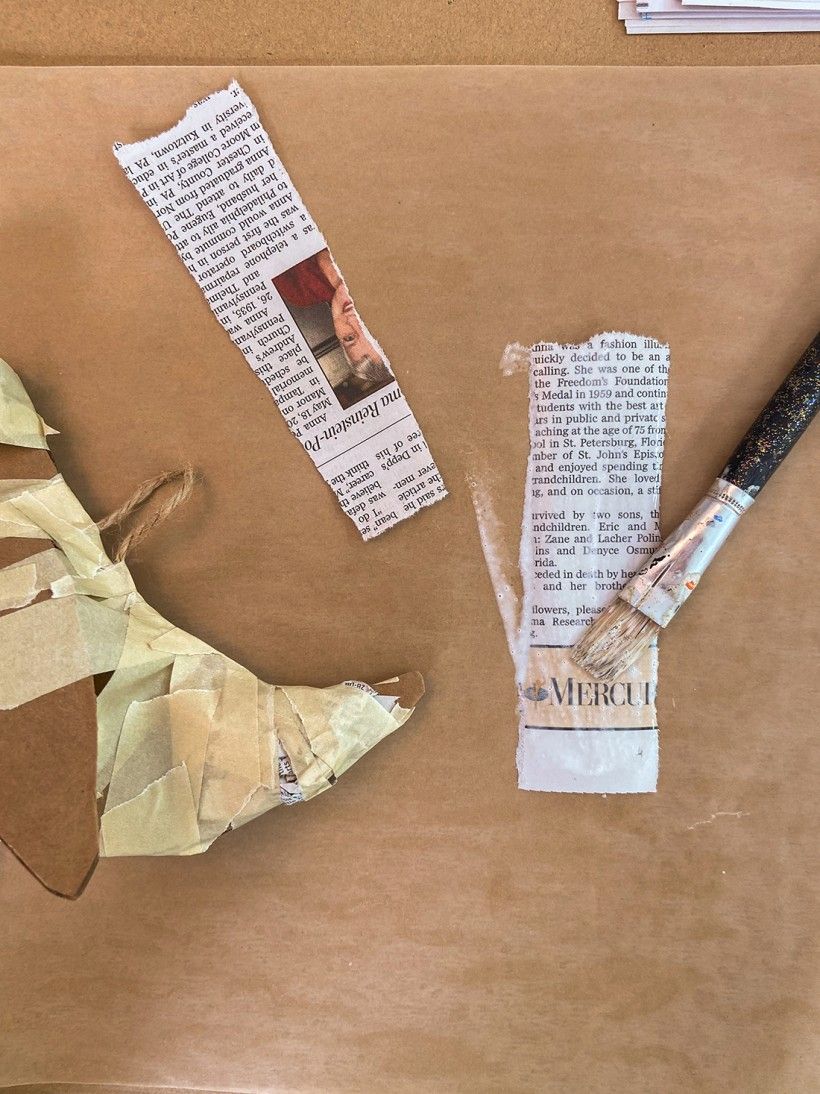 Paintbrush adding glue to strips of newspaper