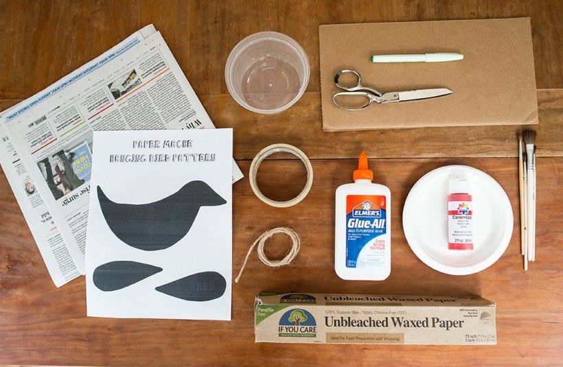 Papier-Mâché supplies, including a bird template, glue, wax paper, scissors, newspaper, cardboard, and paintbrushes