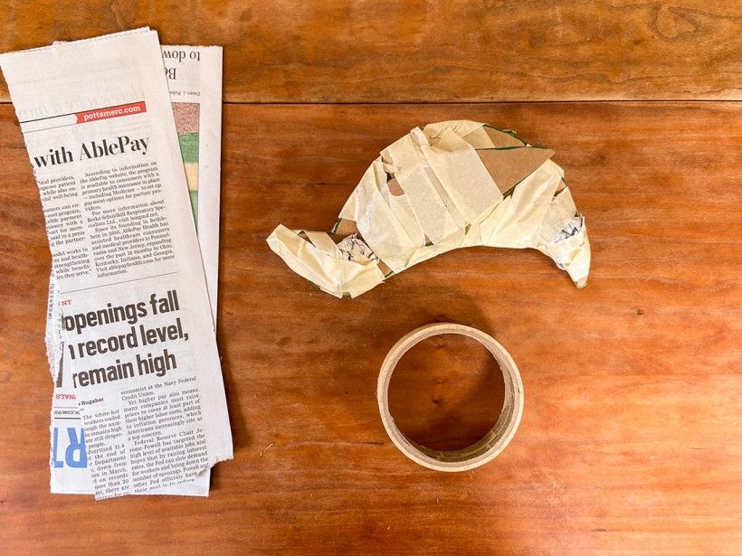 Cardboard cutout of bird wrapped in masking tape pictured next to scraps of newspaper