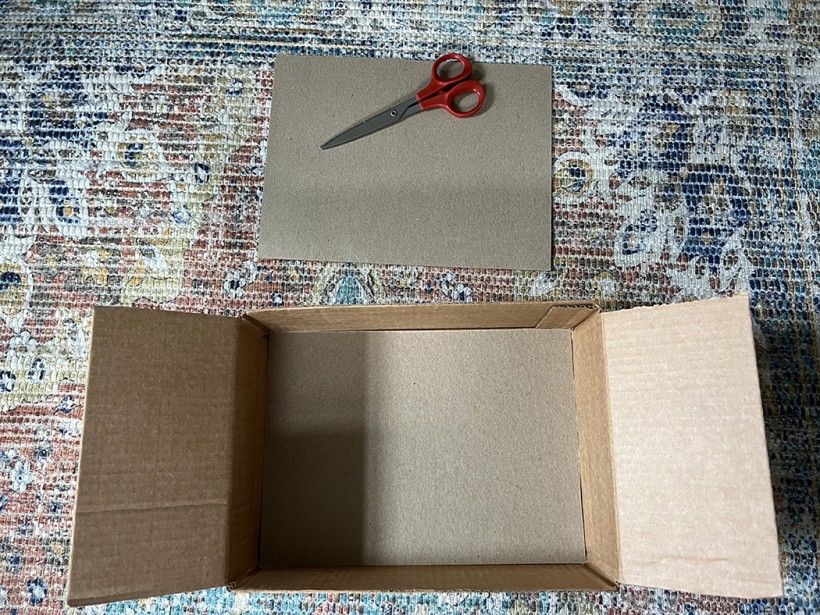 A empty cardboard box, scissors and a piece of thin cardboard cut into a rectangle shape