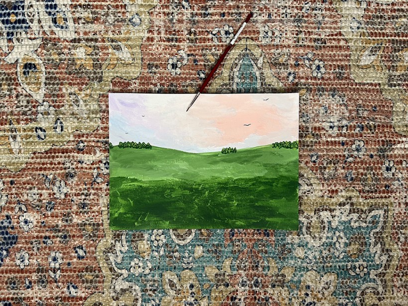 A pastoral scene with grassy fields and a pastel sky painted onto a thin piece of cardboard