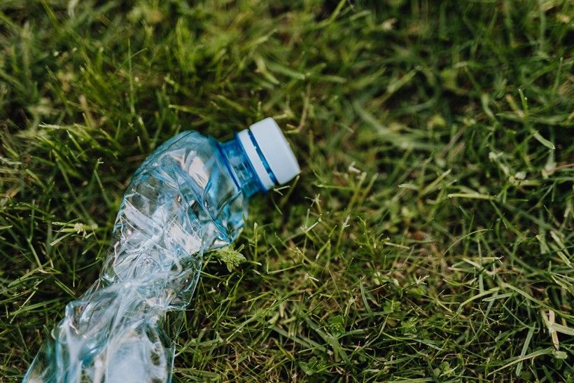Crunched up plastic bottle laying on top of grass. Photo by Karolina Grabowska