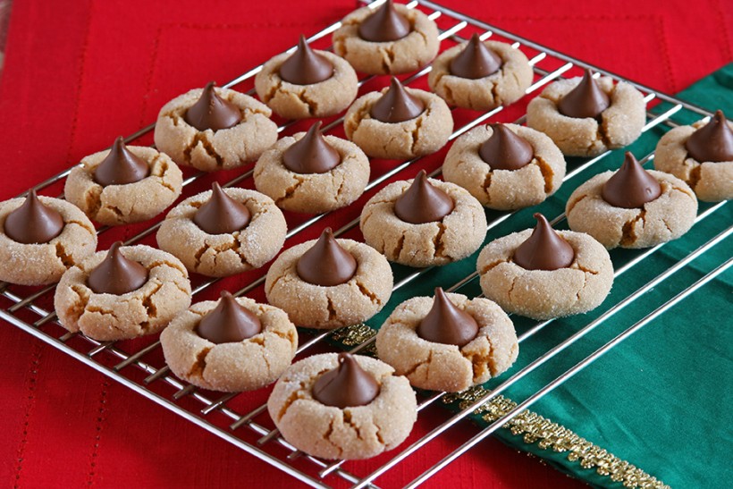 Twenty peanut butter blossom cookies lined up on a cooling tray, pictured on top of a red and green tablecloth
